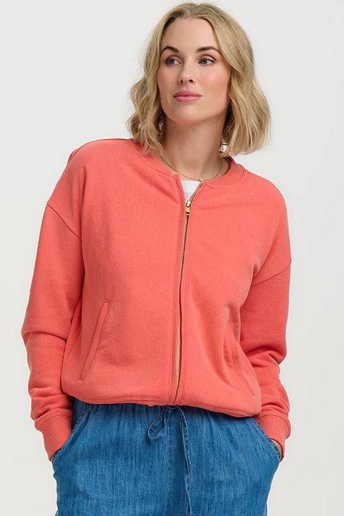 Woman wearing a coral jacket and blue jeans on a white background