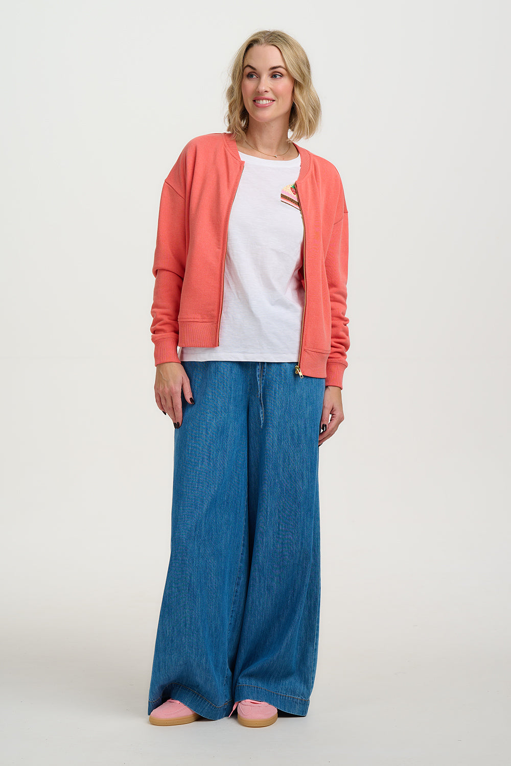 Woman wearing a coral cardigan, white shirt, blue pants, and pink shoes on a white background