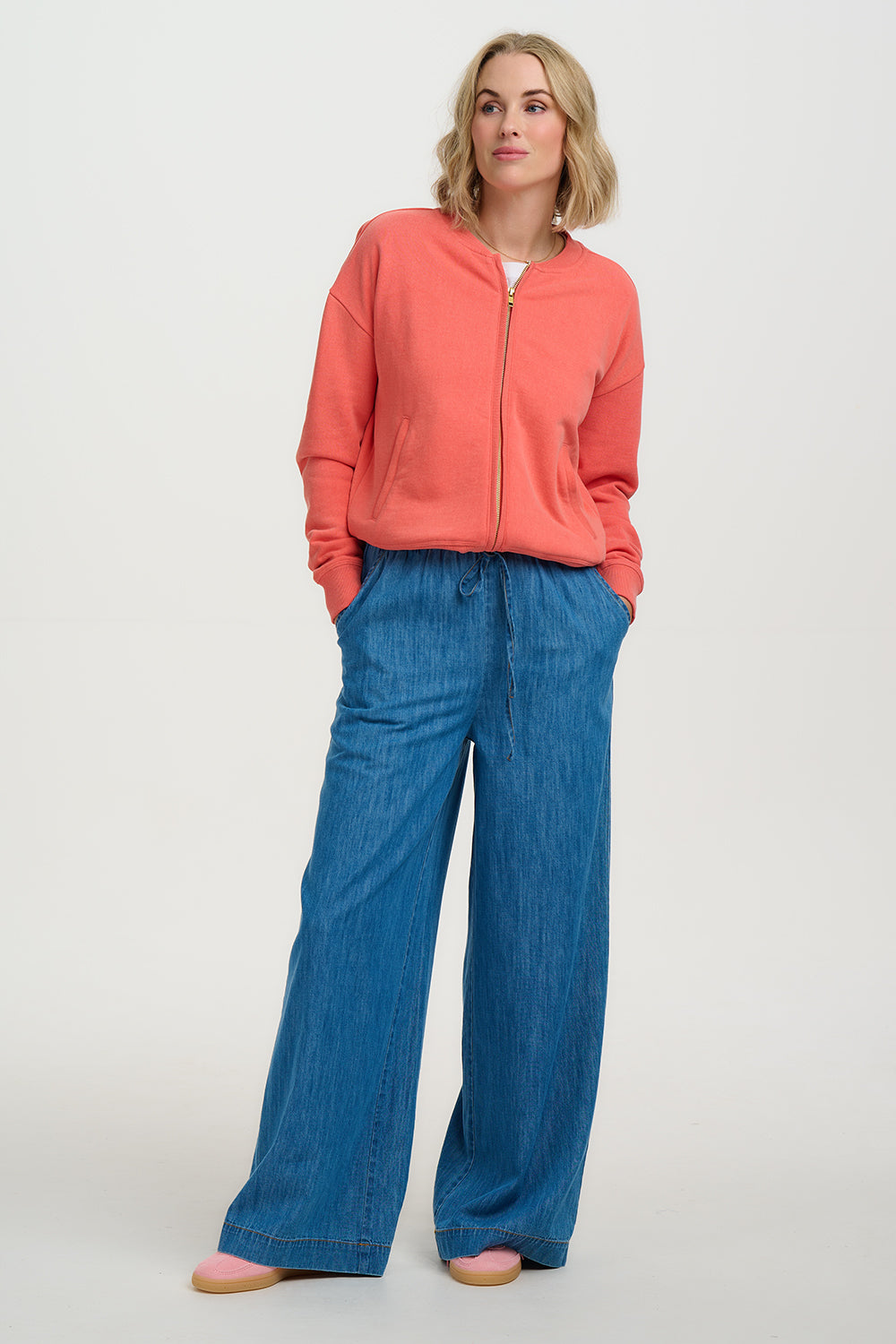 Woman wearing a coral jacket and blue jeans on a white background