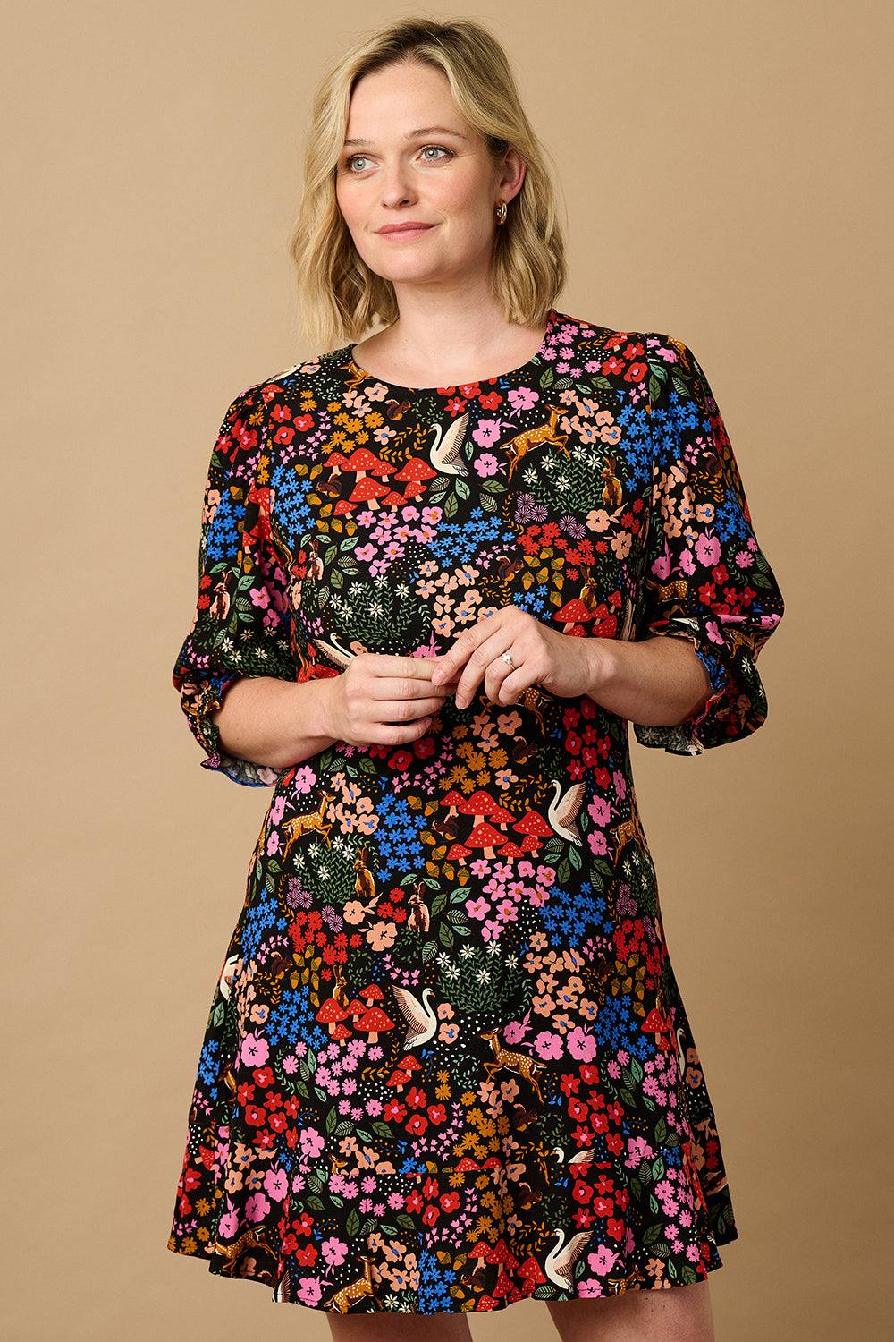 A woman standing and smiling, wearing a multicolored floral dress with half-length blouson sleeves and a frill hem skirt.