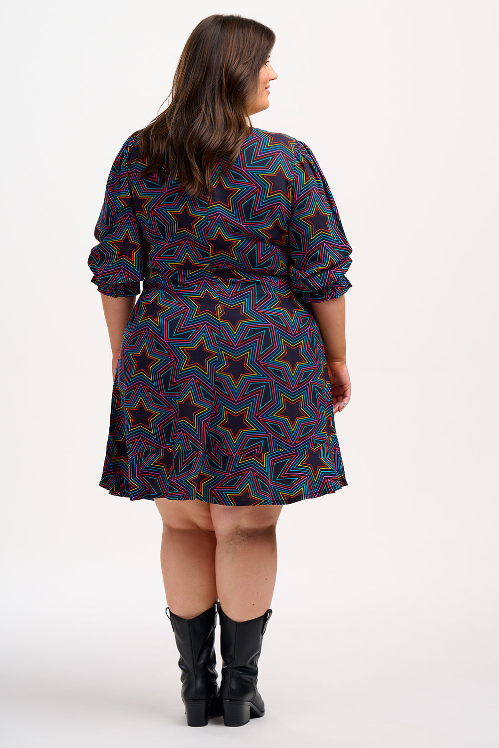 A woman wearing a knee-length black dress with a multicolored star print and long blouson sleeves.