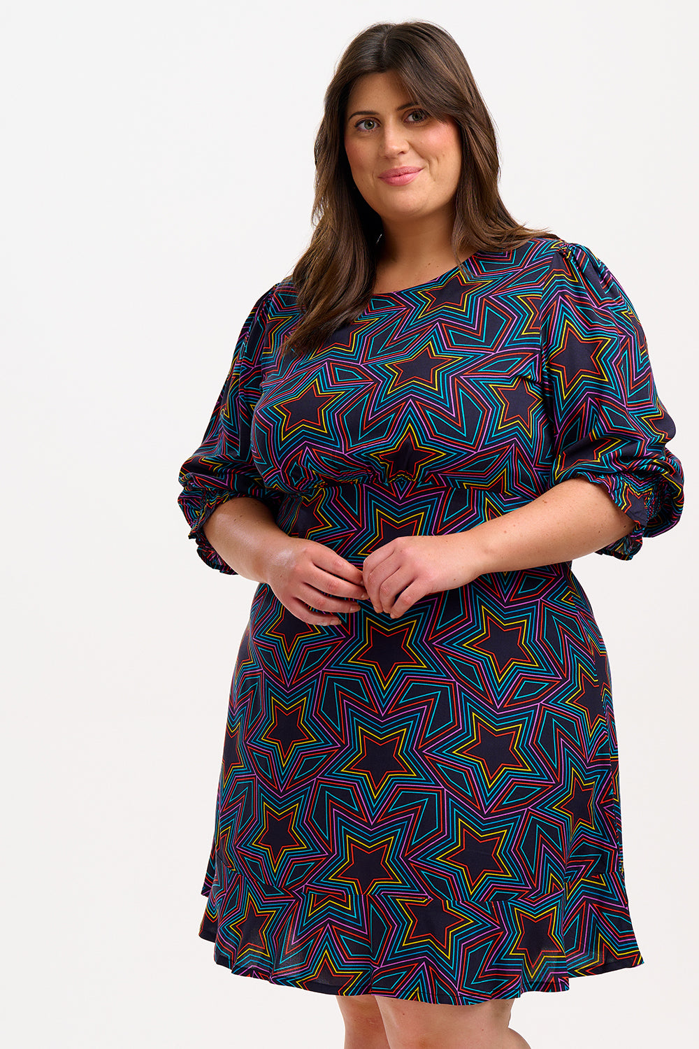 A woman wearing a knee-length black dress with a multicolored star print and long blouson sleeves.