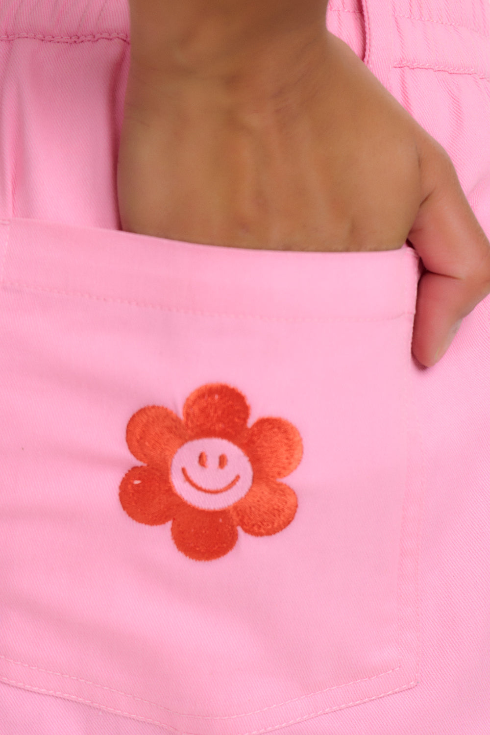 A  wearing bubblegum pink shorts with a smiley flower pocket 