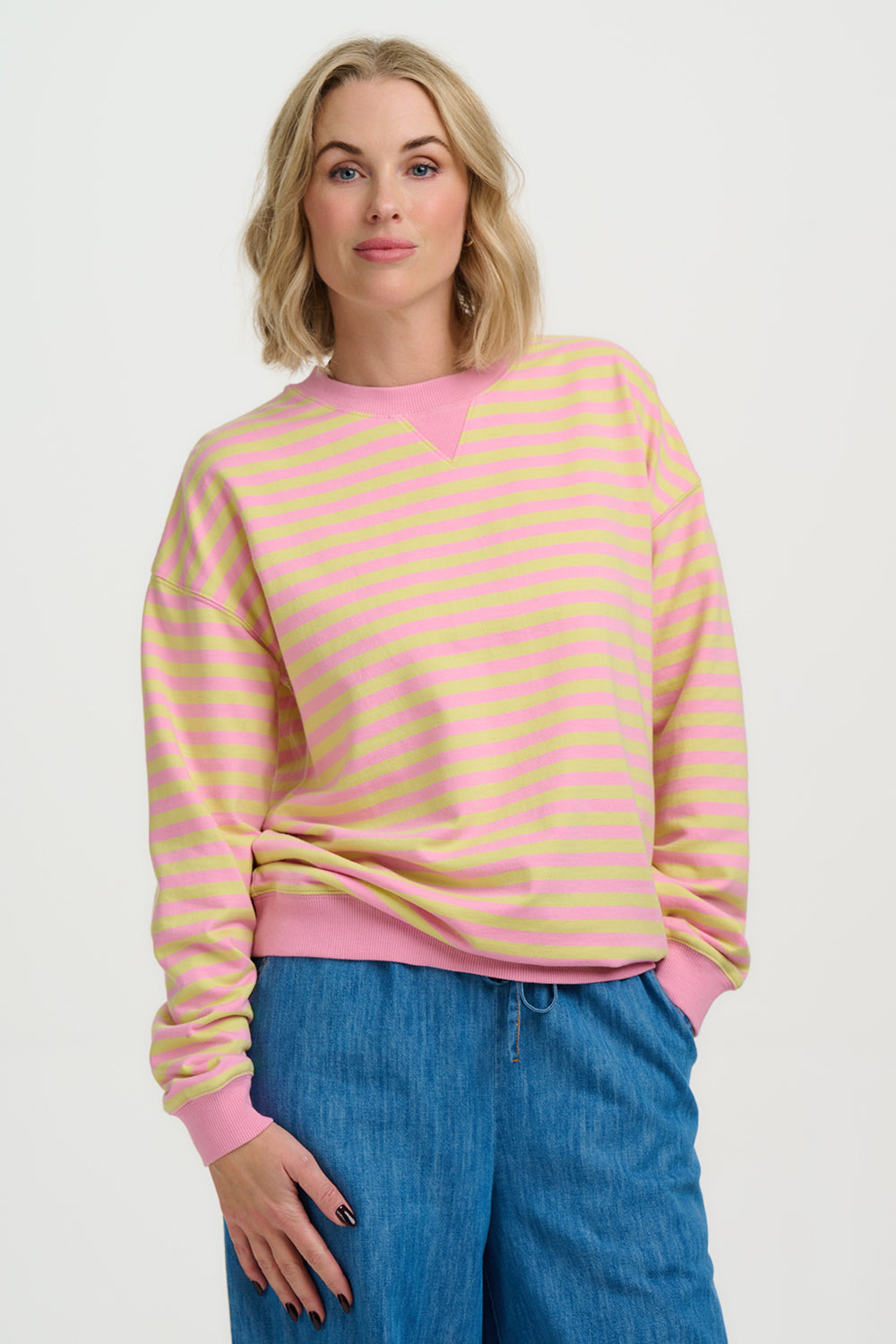 Woman wearing a pink and yellow striped sweater with blue jeans on a white background