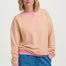 Woman wearing a pink and yellow striped sweater with blue jeans on a white background