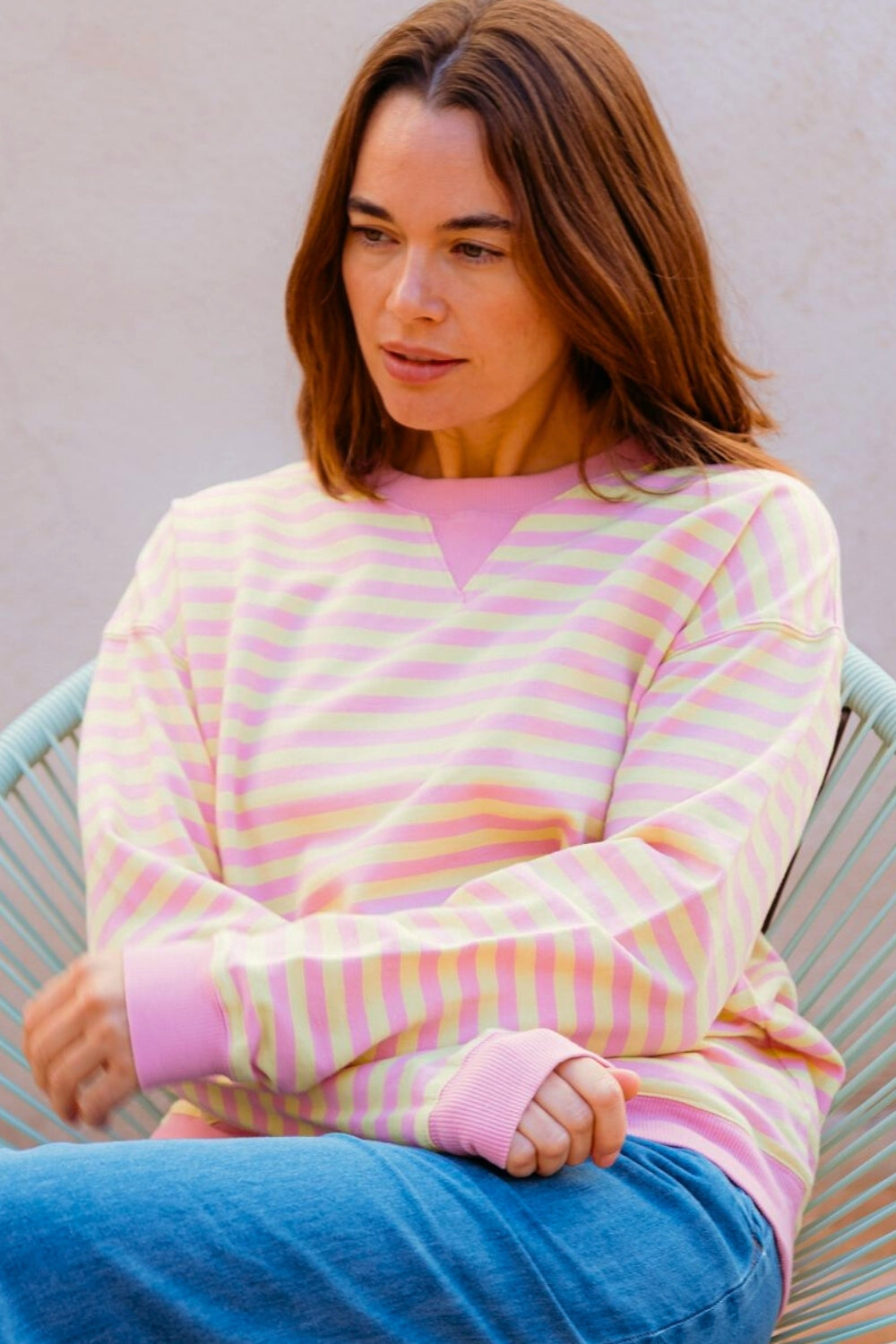 Woman wearing a pink and yellow striped sweater with blue jeans on a white background