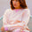 Woman wearing a pink and yellow striped sweater with blue jeans on a white background