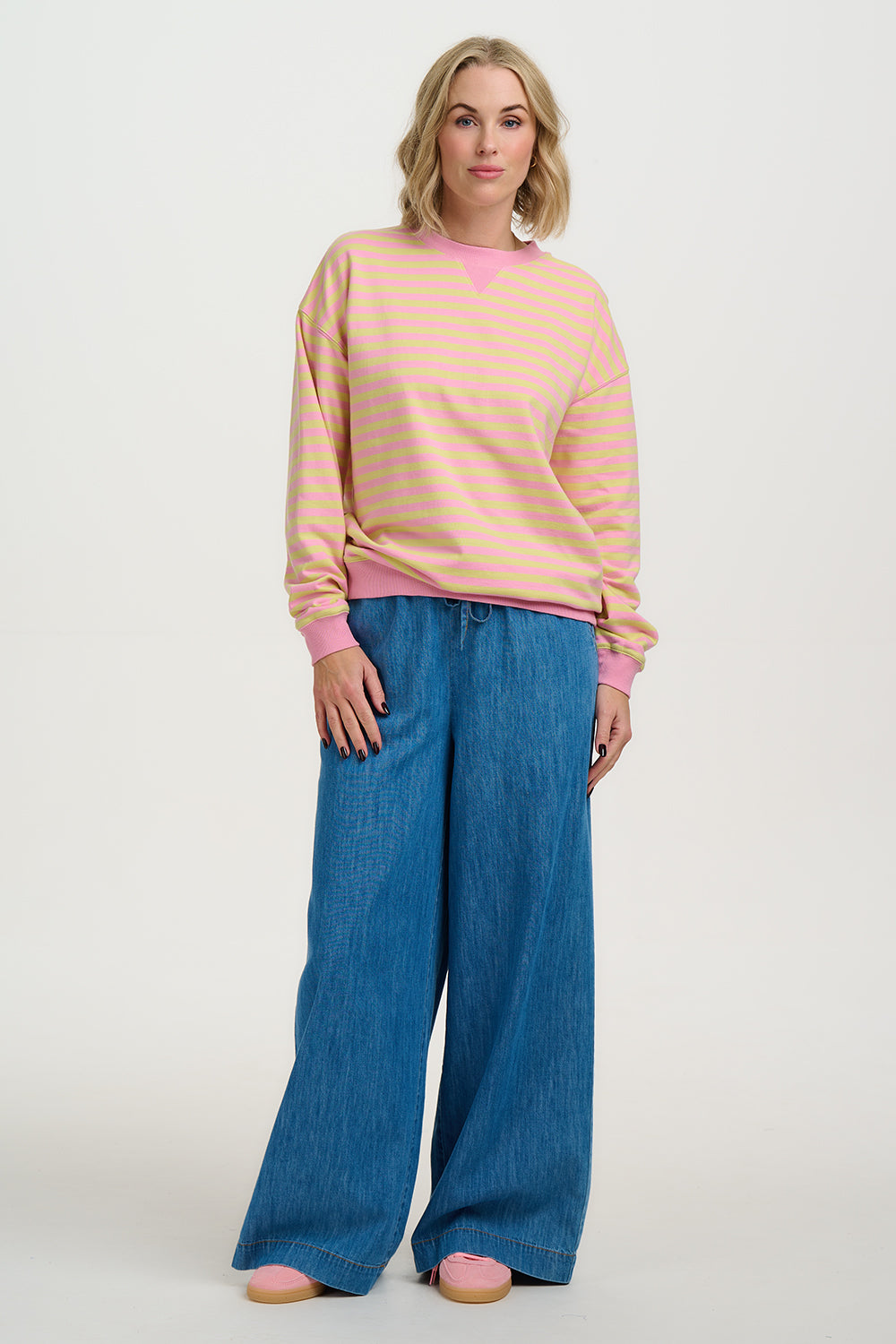 Woman wearing a peach striped sweater and blue pants on a white background