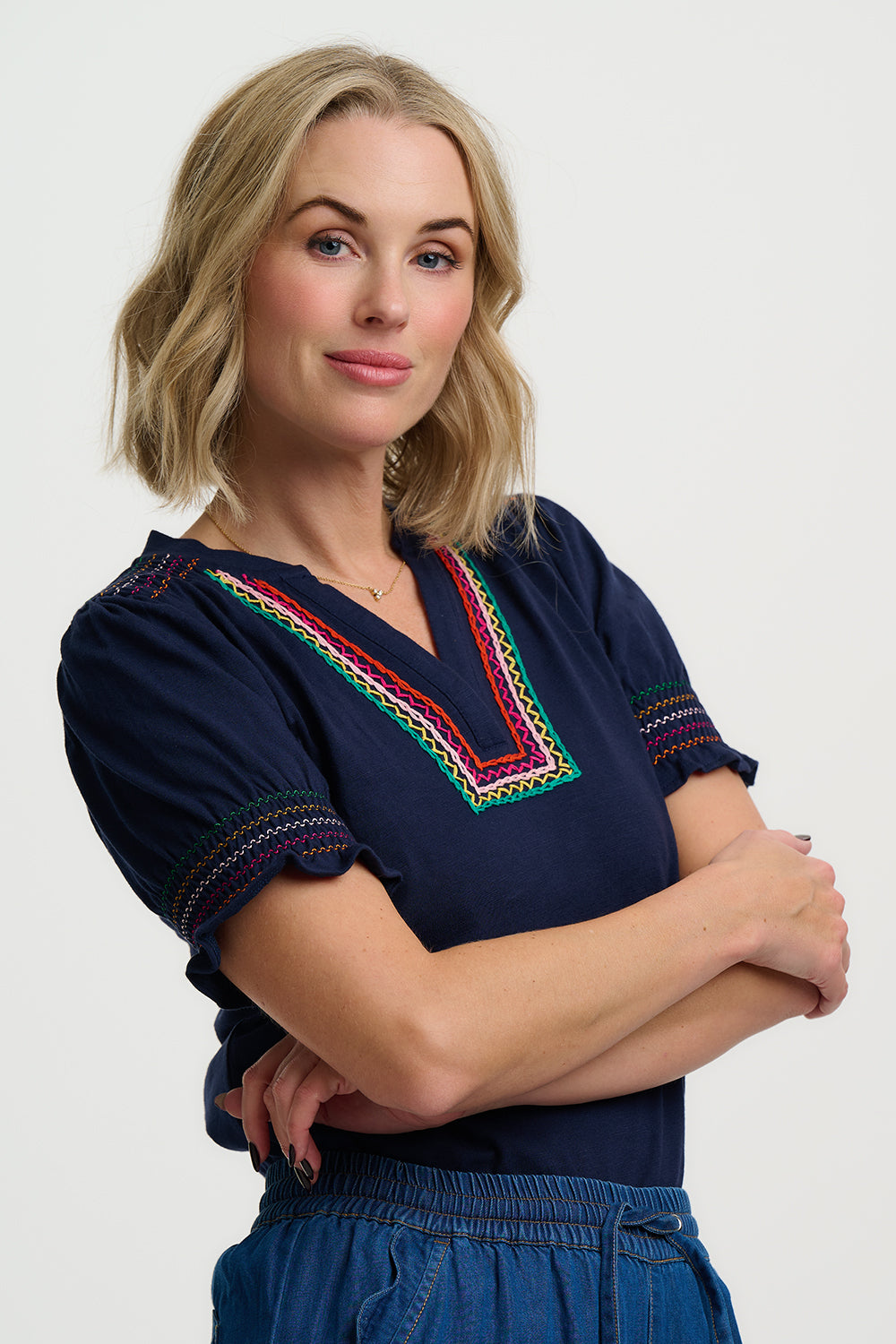 Woman wearing a navy blue top with colorful embroidery on a white background
