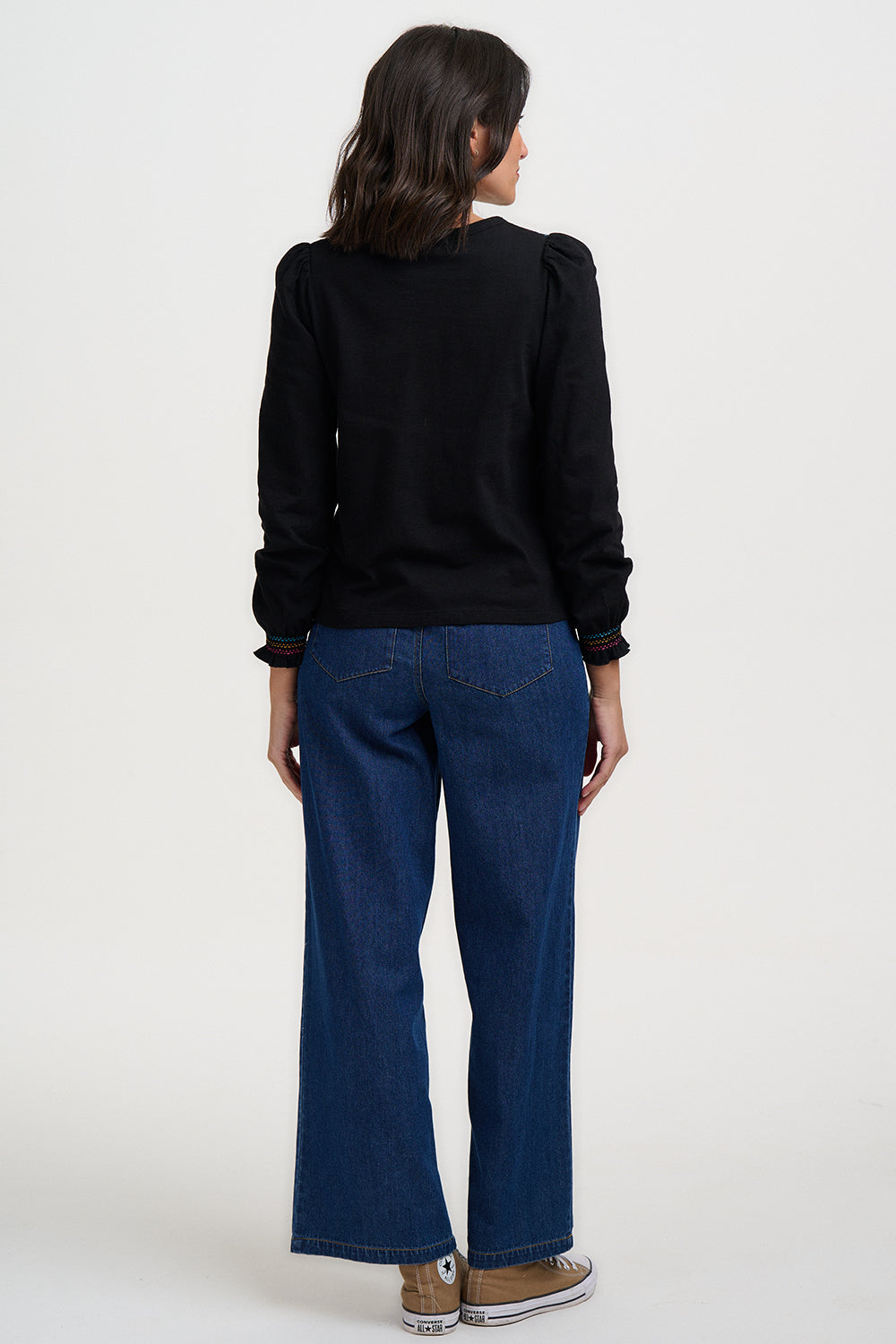 Person wearing a black sweater and blue jeans on a white background