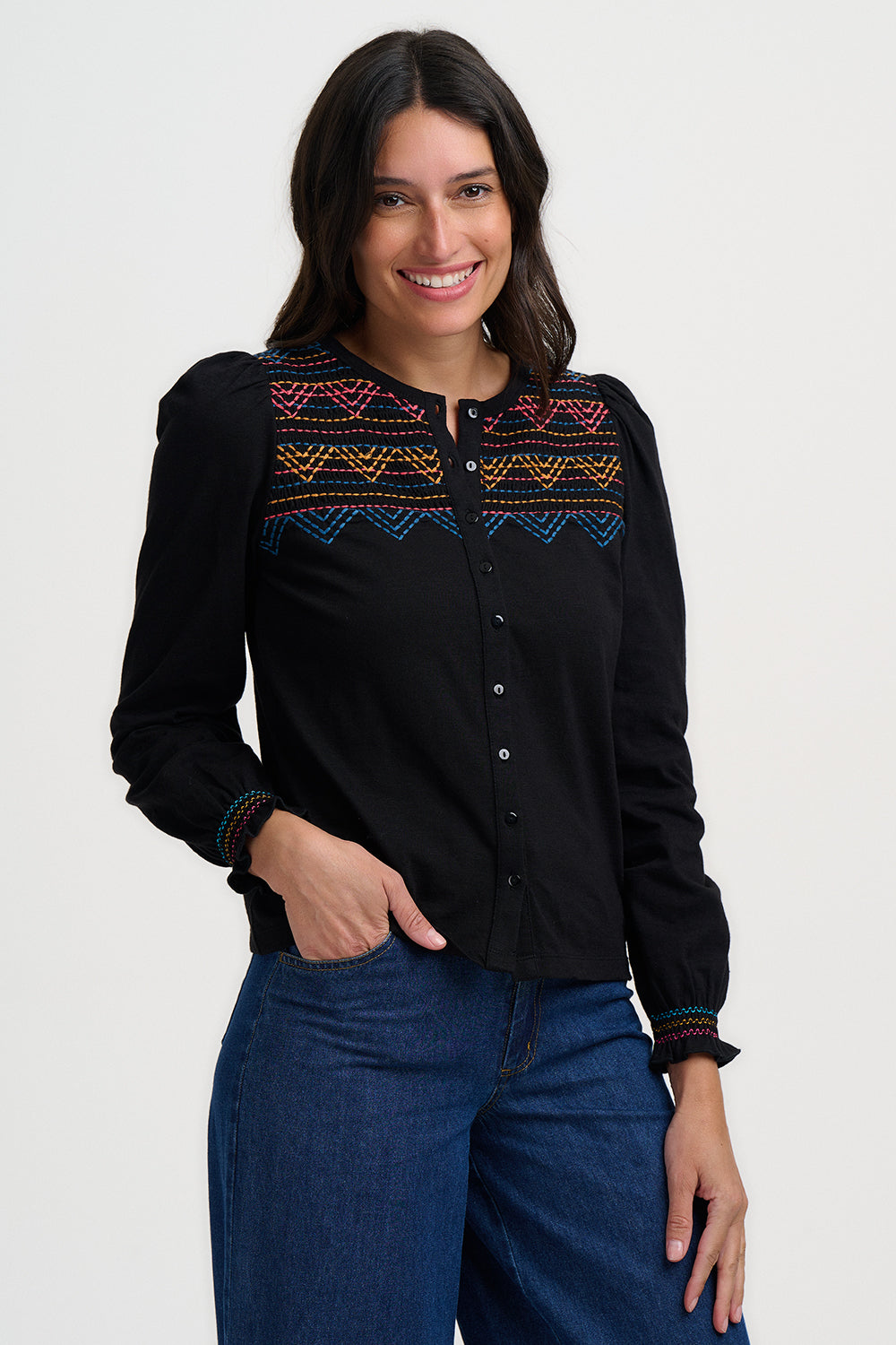 Woman wearing a black blouse with colorful patterns and blue jeans on a white background