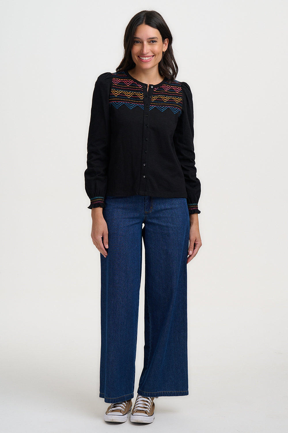 Woman wearing a black embroidered shirt and blue jeans on a white background