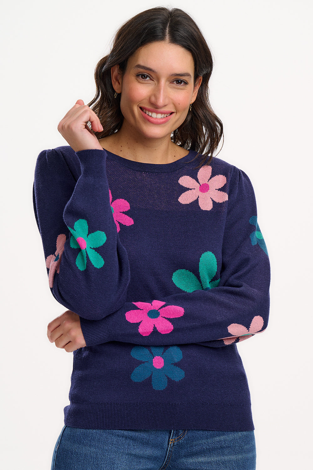 A woman wearing a navy blue jumper with a floral pattern consisting of large flowers in pink and green, paired with jeans.