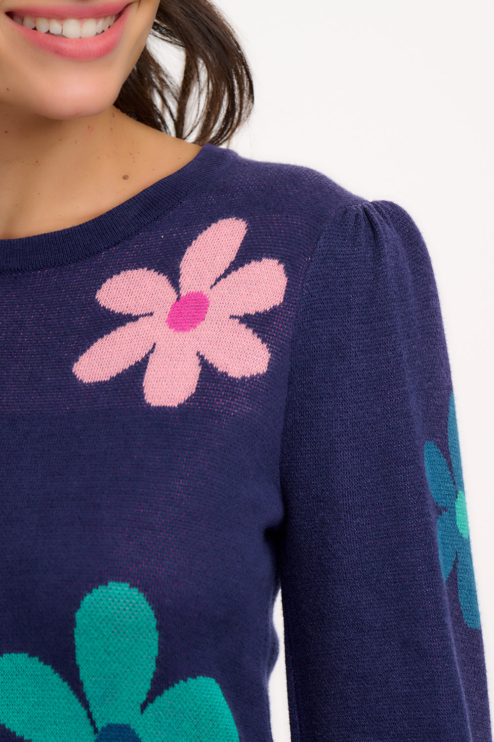 A woman wearing a navy blue jumper with a floral pattern consisting of large flowers in pink and green, paired with jeans.