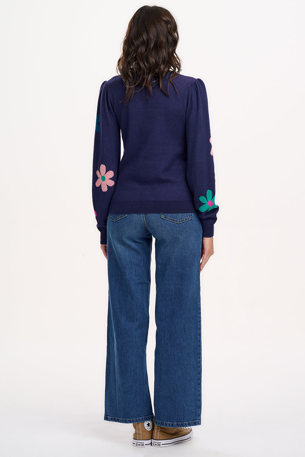 A woman wearing a navy blue jumper with a floral pattern consisting of large flowers in pink and green, paired with jeans.