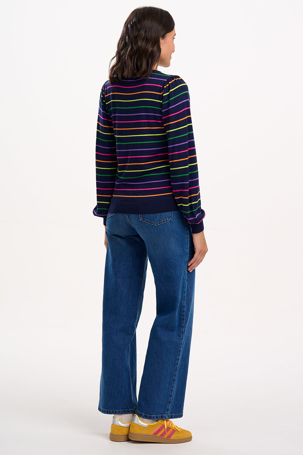 Sugarhill Brighton model wearing a colorful striped sweater and blue jeans on a white background