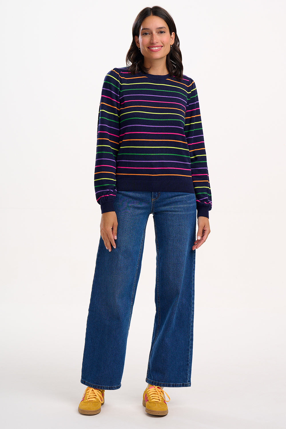 Sugarhill Brighton model wearing a striped sweater and blue jeans on a white background