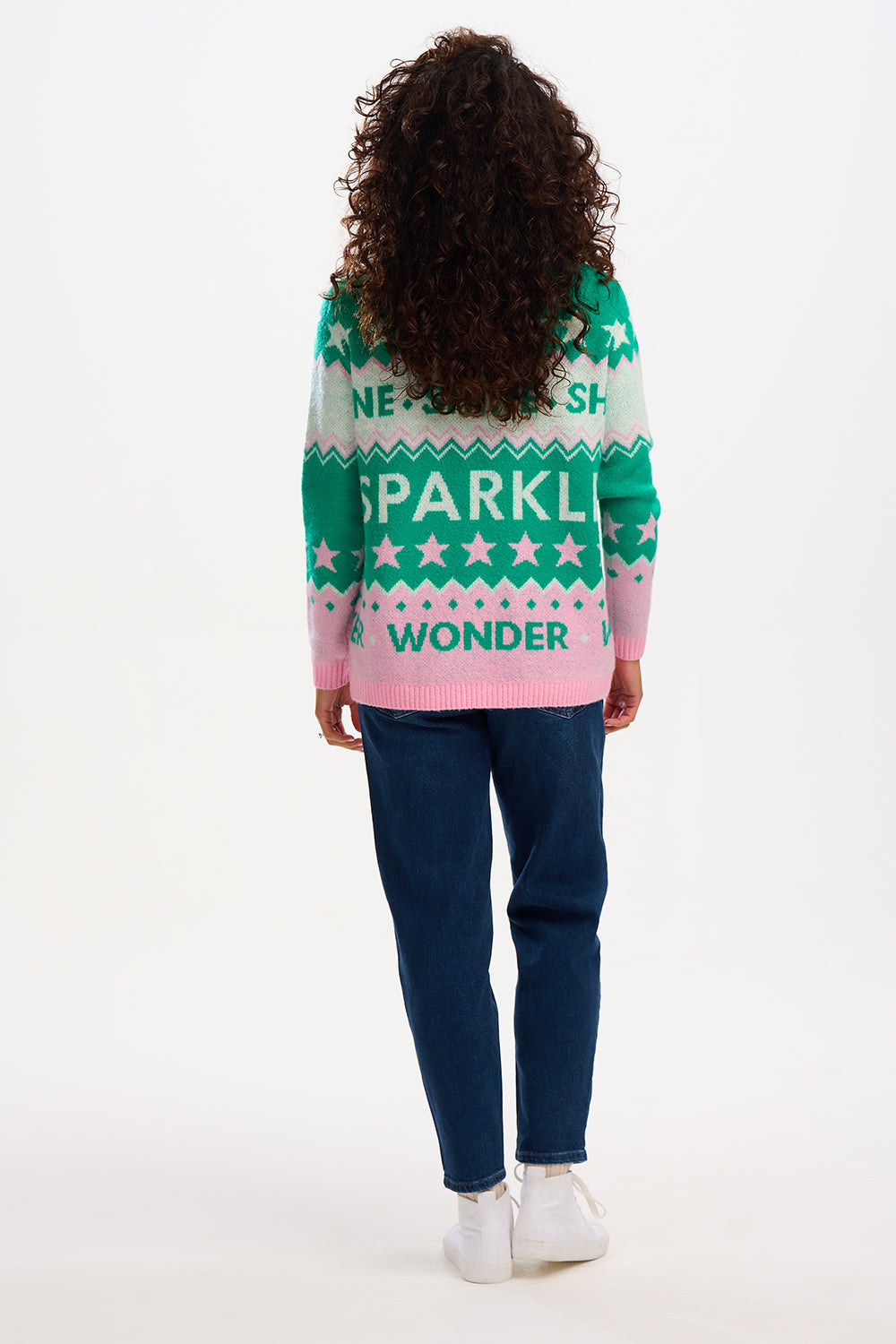 Woman wearing a festive sweater with 'Shine' and 'Sparkle' text, standing outdoors.