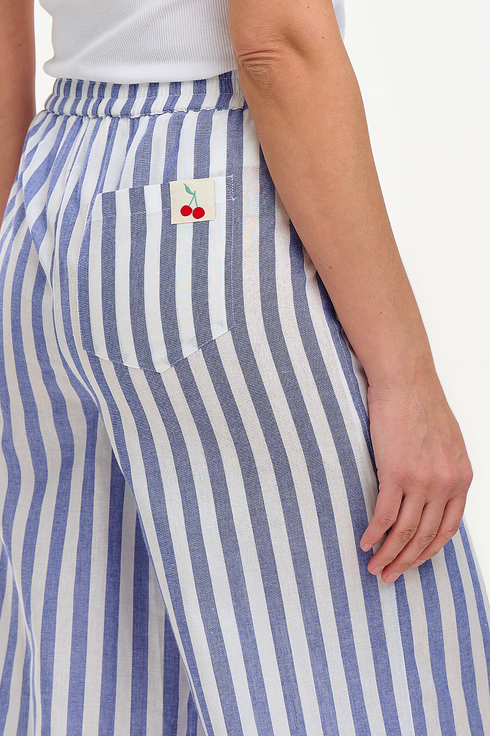 A woman modeling wide leg cropped trousers with an all-over bakers stripe in white and blue, paired with a white t-shirt and white sandals.