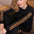A woman with red hair sits on a brown leather couch wearing a black long-sleeve top and matching pants with leopard print stripes down the sleeves and along the hem.