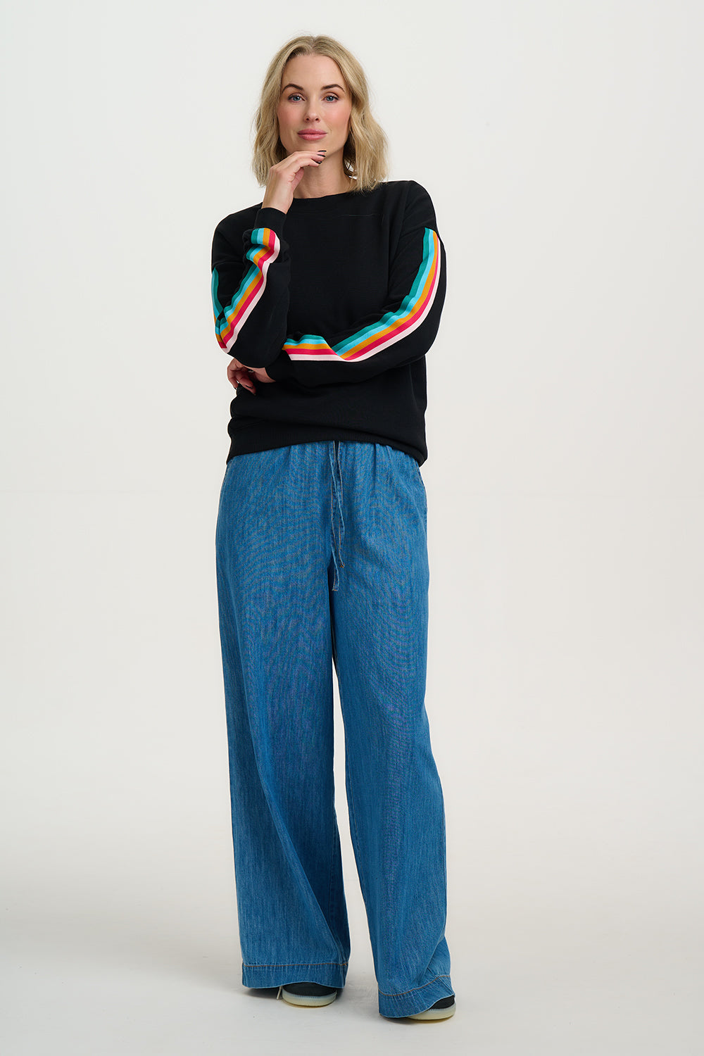 Woman wearing a black sweater with colorful stripes and blue pants on a white background