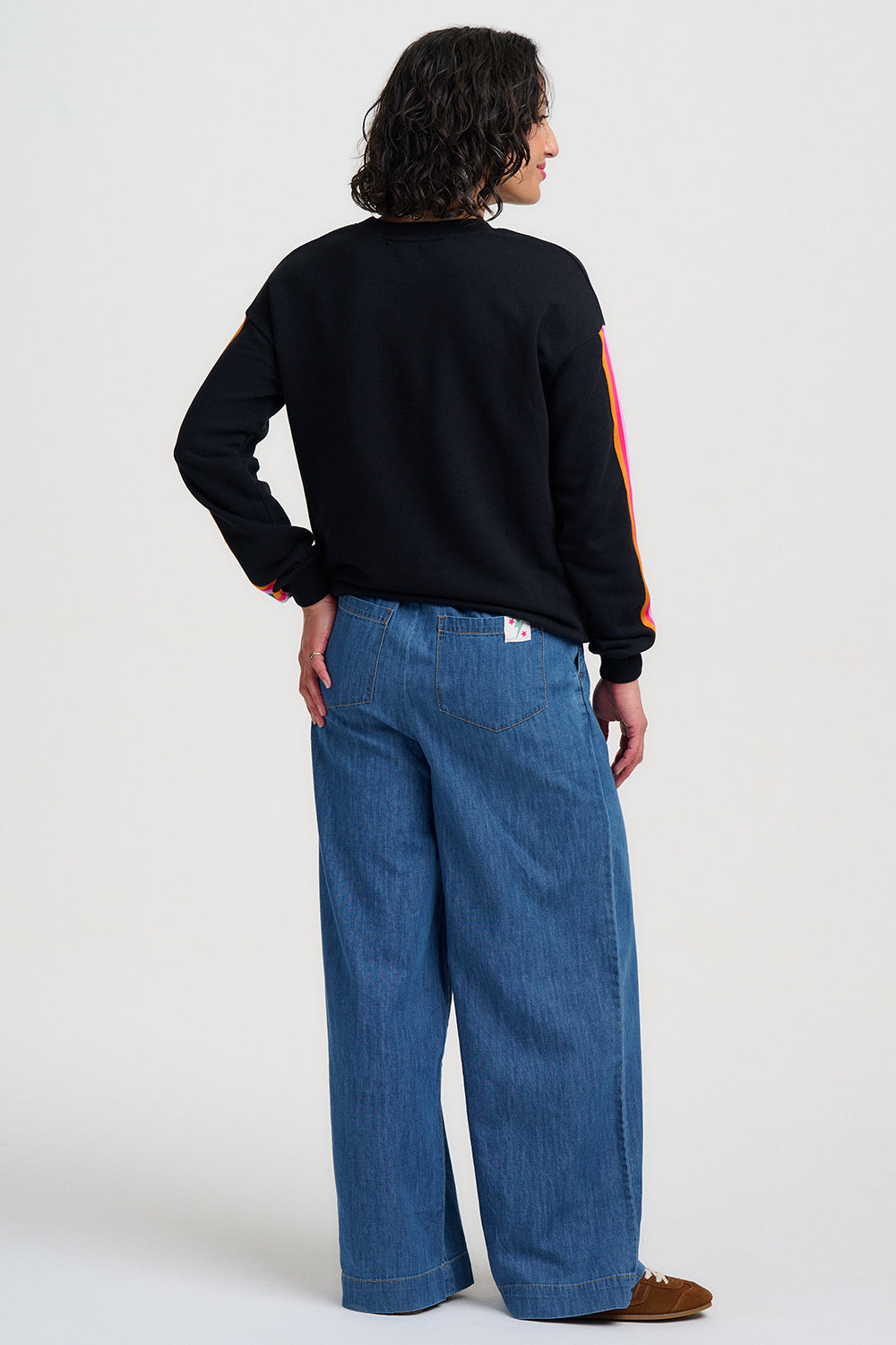 Person wearing a black sweatshirt with colorful sleeves and blue jeans on a white background
