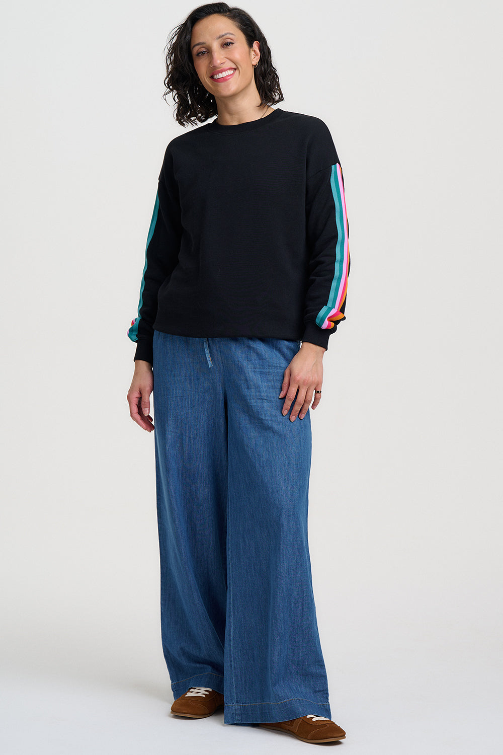 Woman wearing a black sweater with colorful sleeves and blue pants on a white background