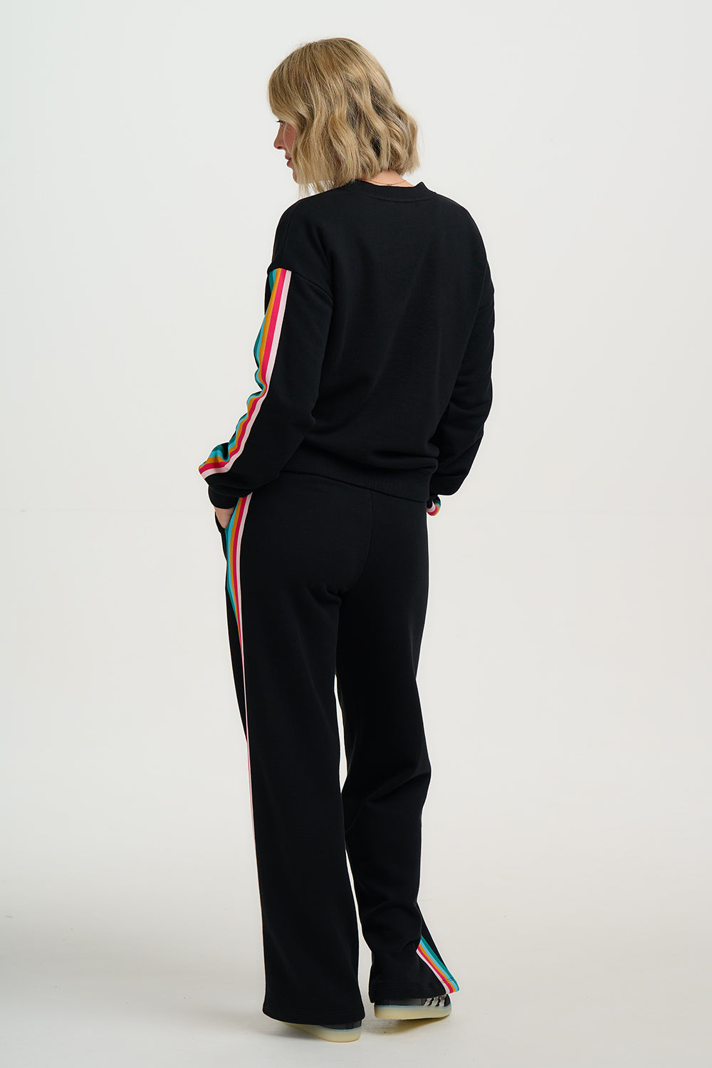 Person wearing a black tracksuit with colorful side stripes on a white background