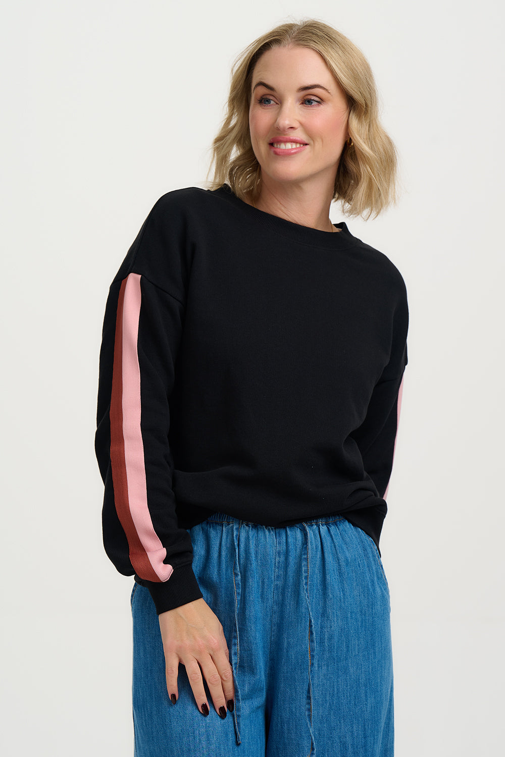 Woman wearing a black sweater with pink sleeves and blue jeans on a white background