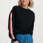 Woman wearing a black sweater with pink sleeves and blue jeans on a white background