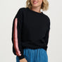 Woman wearing a black sweater with pink sleeves and blue jeans on a white background