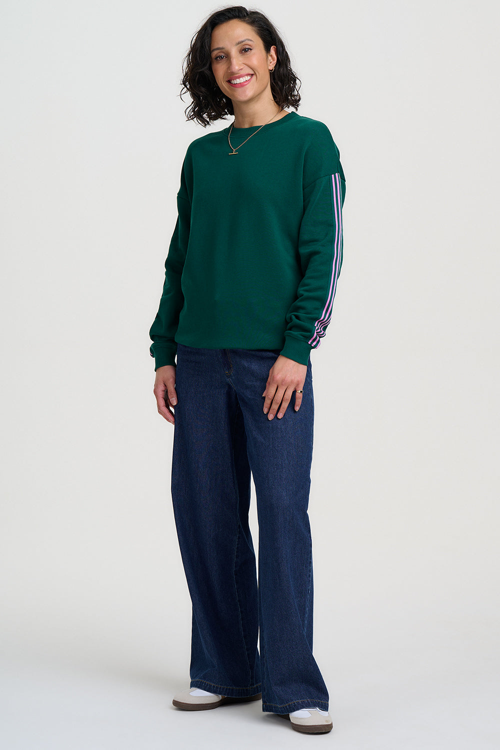 Woman wearing a green sweater with striped sleeves and blue jeans on a white background