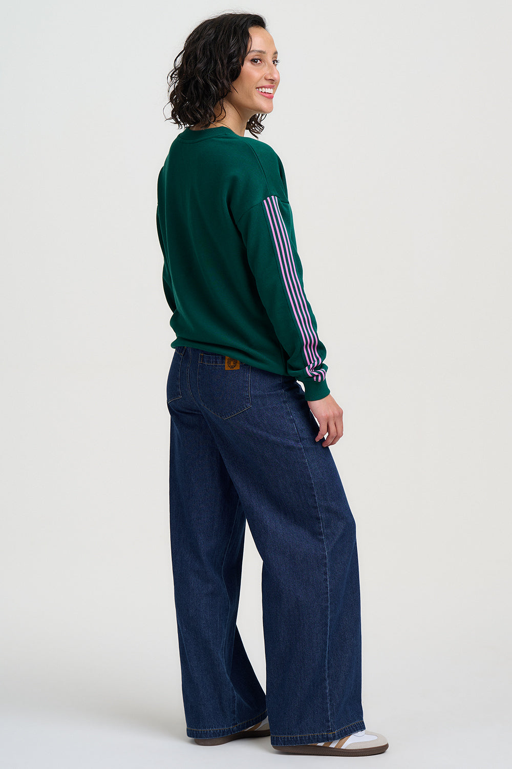 Woman wearing a green sweater with pink stripes and blue jeans on a white background