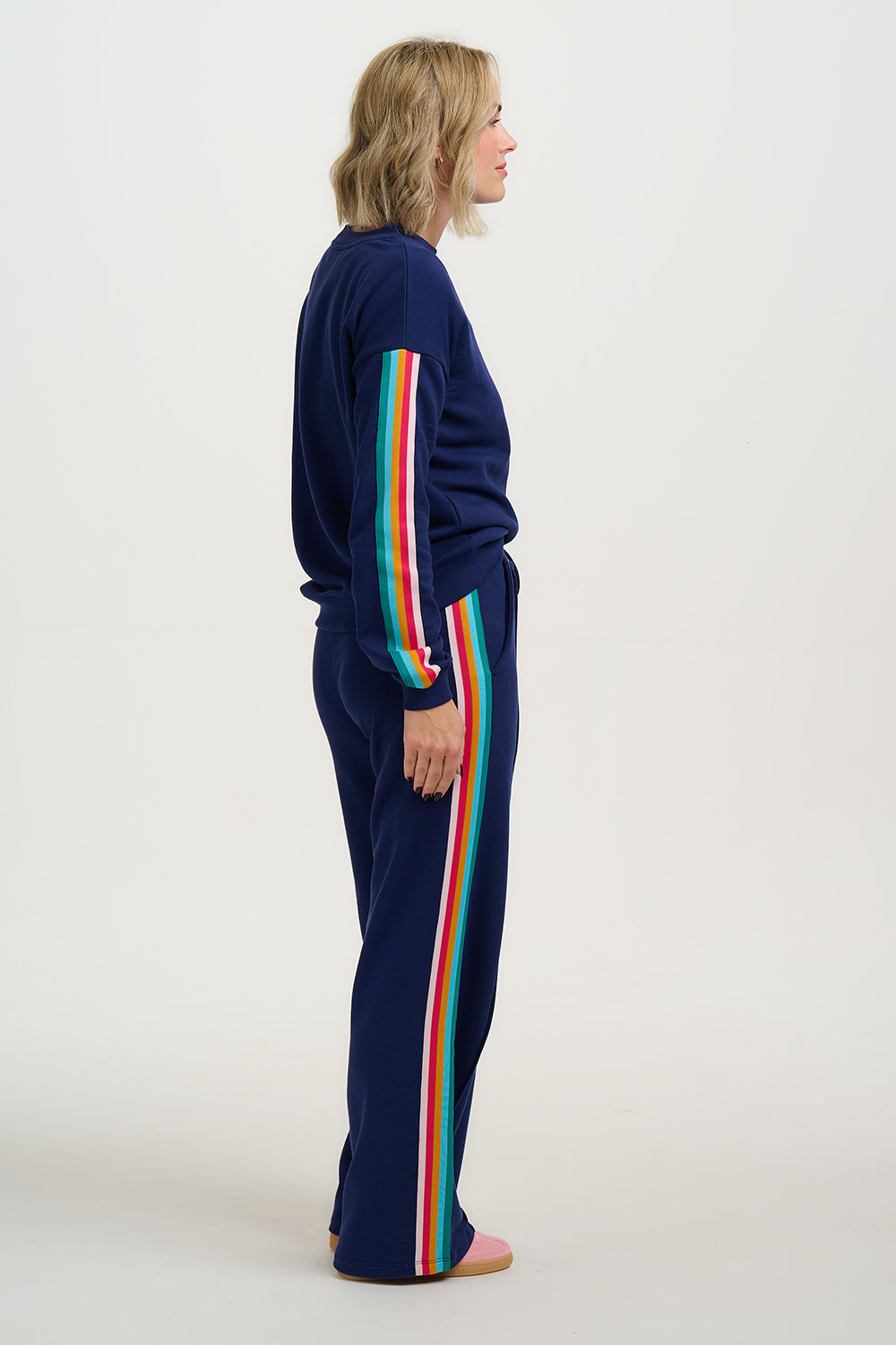 Person wearing a navy tracksuit with rainbow stripes on a white background