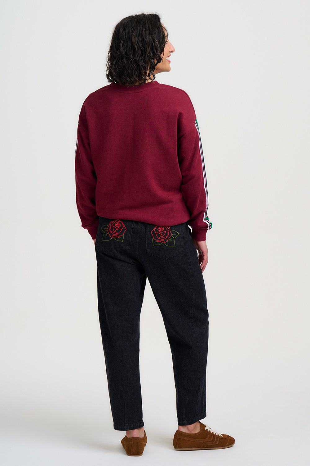 Person wearing a burgundy sweater and black pants with floral embroidery on a white background