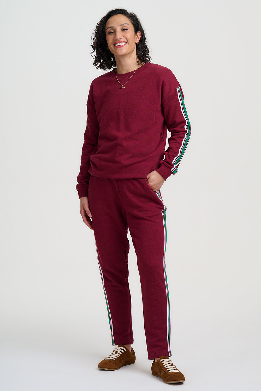 Person wearing a burgundy tracksuit with green stripes on a white background