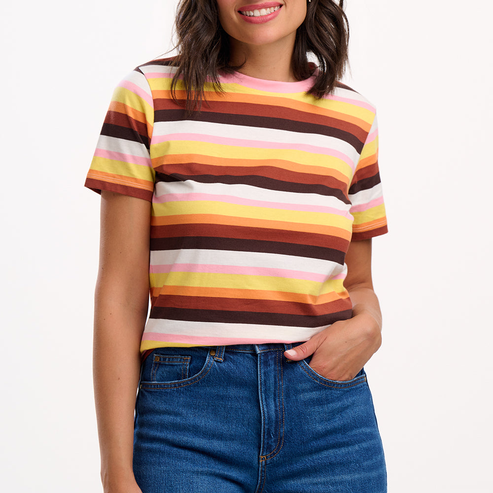 Sugarhill Brighton model wearing a colourful striped shirt and blue jeans on a white background
