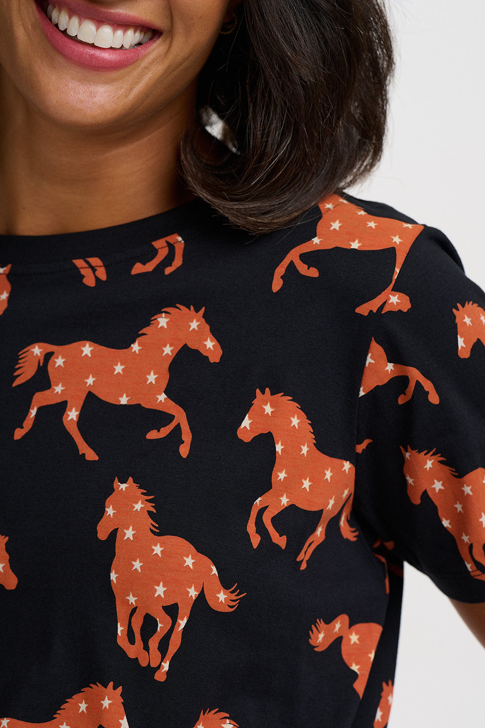 Close-up of a woman wearing a black short-sleeve top with an all-over orange horse print decorated with small white stars.