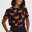 A woman wearing a black short-sleeve t-shirt with an all-over print of brown horses with white spots, paired with dark denim jeans, against a light gray studio background.