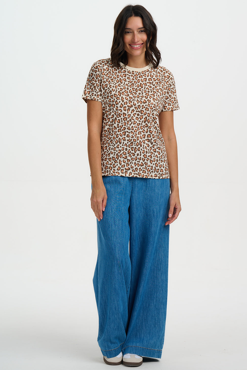 Woman wearing a leopard print top and blue pants on a white background