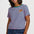 A woman wearing a short-sleeve striped t-shirt with pink and teal horizontal stripes, featuring a small embroidered leopard on the left chest. She is also wearing blue jeans against a plain light gray studio background.