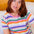 Woman wearing a colorful striped shirt sitting on a couch.