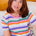 Woman wearing a colorful striped shirt sitting on a couch.