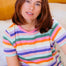 Woman wearing a colorful striped shirt sitting on a couch.