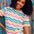 A woman smiling and wearing a multicolored wavy rainbow stripe t-shirt with a crew neck.