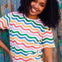 A woman smiling and wearing a multicolored wavy rainbow stripe t-shirt with a crew neck.
