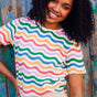 A woman smiling and wearing a multicolored wavy rainbow stripe t-shirt with a crew neck.
