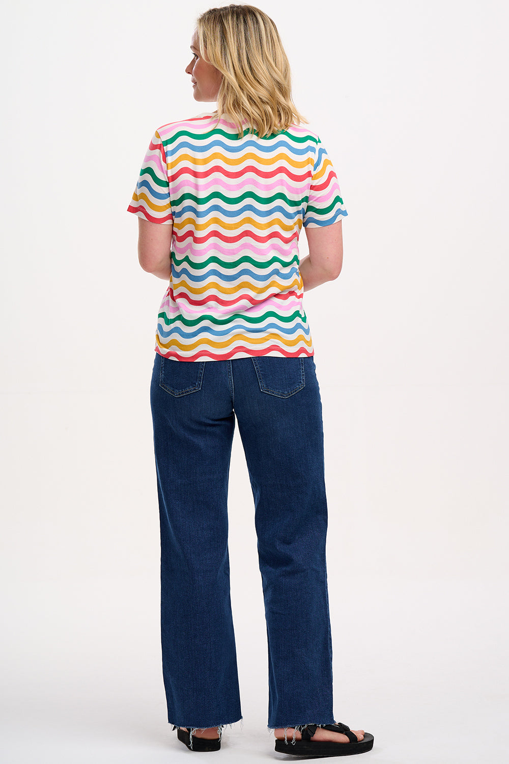 A woman smiling and wearing a multicolored wavy rainbow stripe t-shirt with a crew neck.