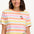 A woman modeling a multicolored striped t-shirt with a small embroidered cherry on the chest, paired with a blue denim skirt.