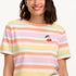 A woman modeling a multicolored striped t-shirt with a small embroidered cherry on the chest, paired with a blue denim skirt.